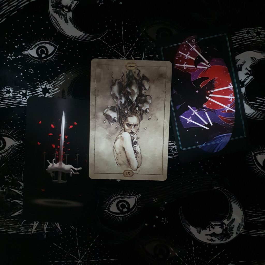 a photo of nine of swords from the true black tarot, hush tarot, and children of litha tarot