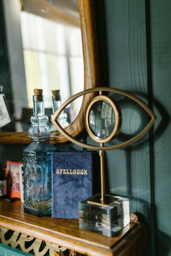 photo of spellbook on shelf with mirror, bottle, and glass eye