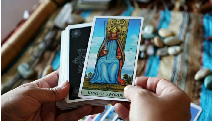 a photo of a tarot reader holding a tarot deck revealing the king of swords tarot court card